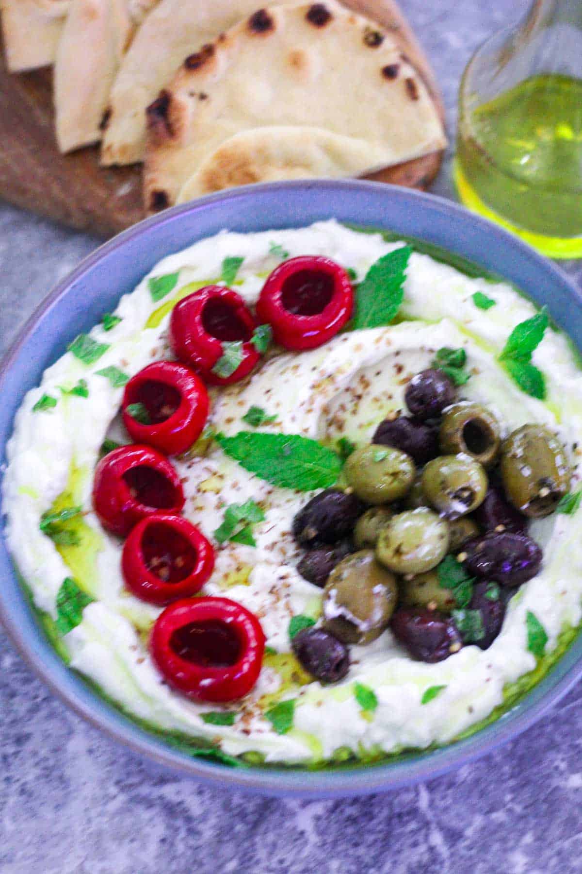 A bowl with whipped cottage cheese dip and feta, topped with olives, mint, za'atar, olive oil and marinated red peppers. 