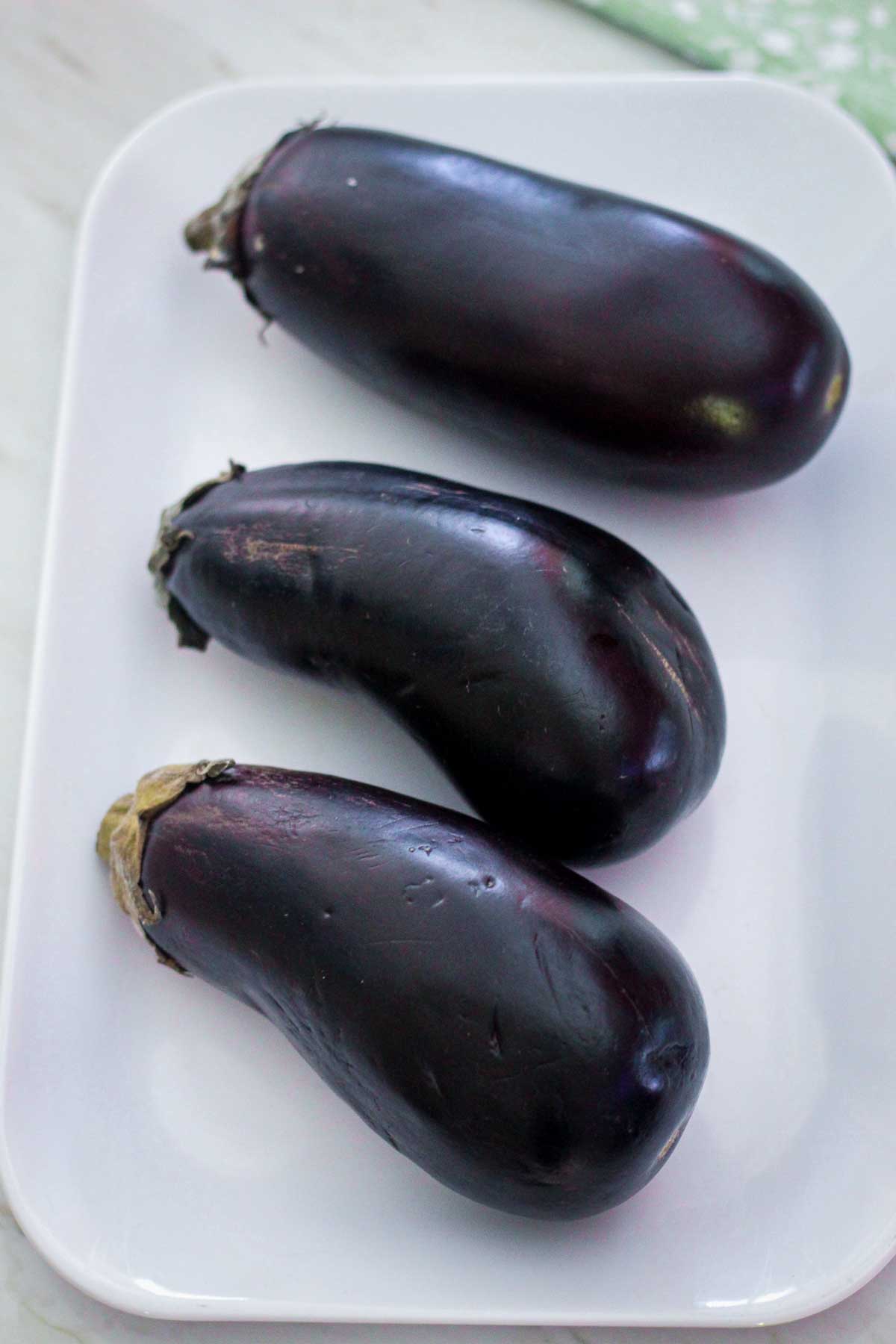 Three eggplants on a white tray.