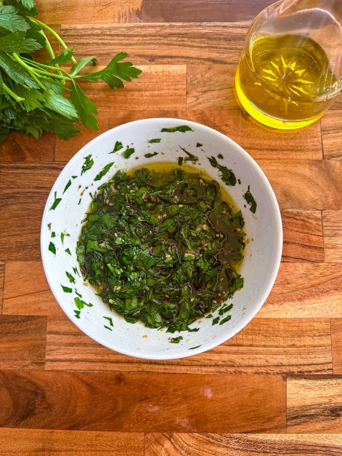 Za'atar and parsley sauce in a white bowl, there's fresh parsley and olive oil in a container next to the bowl.