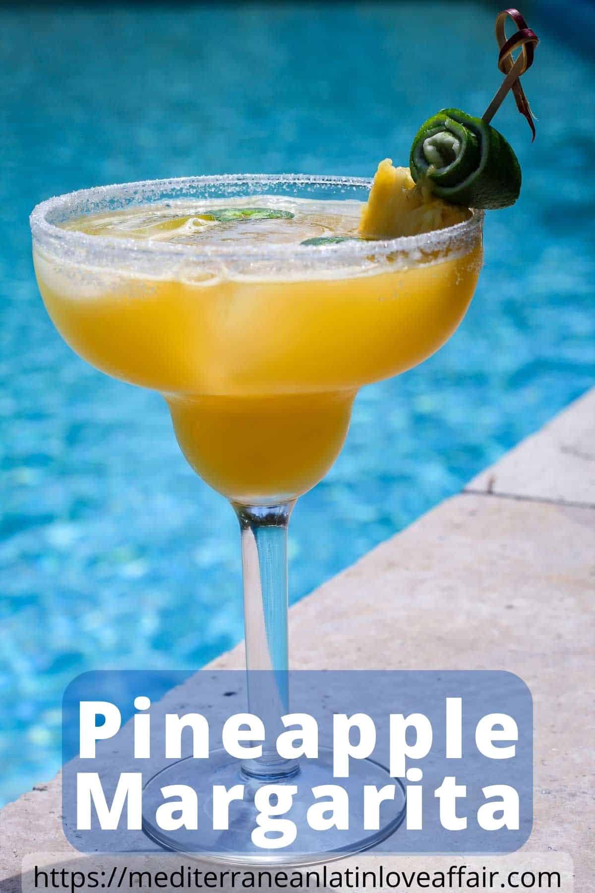 An image prepared for Pinterest, it shows a margarita glass next to the pool. Glass is garnished with pineapple and lime, while slices of jalapenos are seen floating on the drink. 