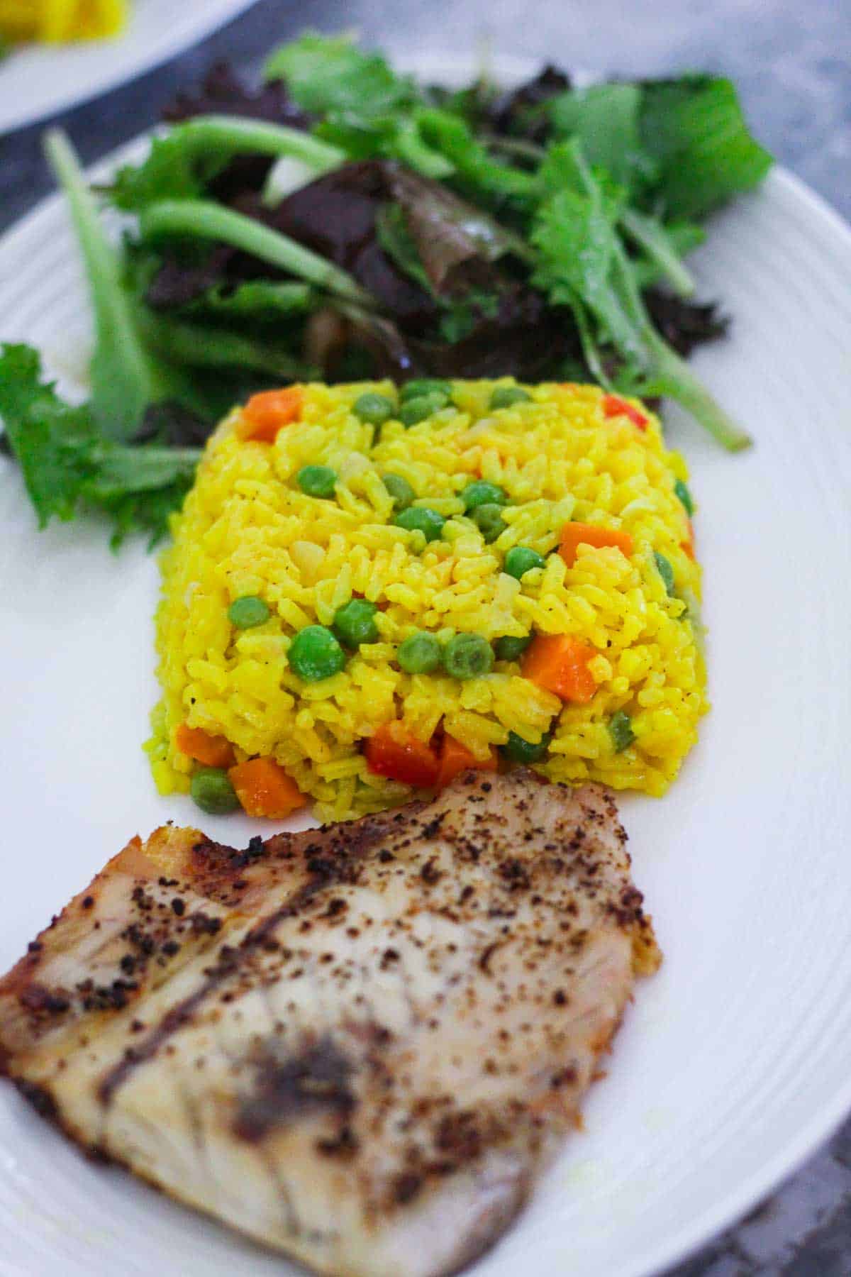 A platter with saffron rice, a white fish and salad. 