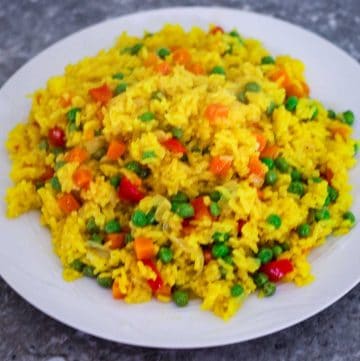 A white round plate with lots of yellow rice with veggies.