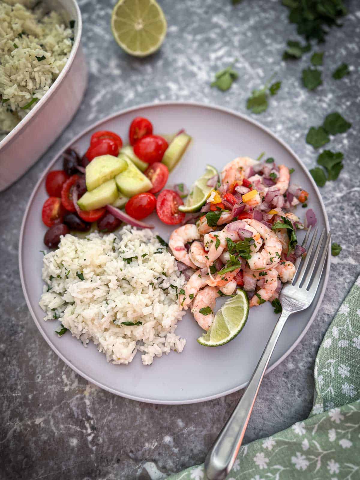 A plate shown with cilantro, lime rice, a tomato and cucumber salad and some shrimp ceviche.