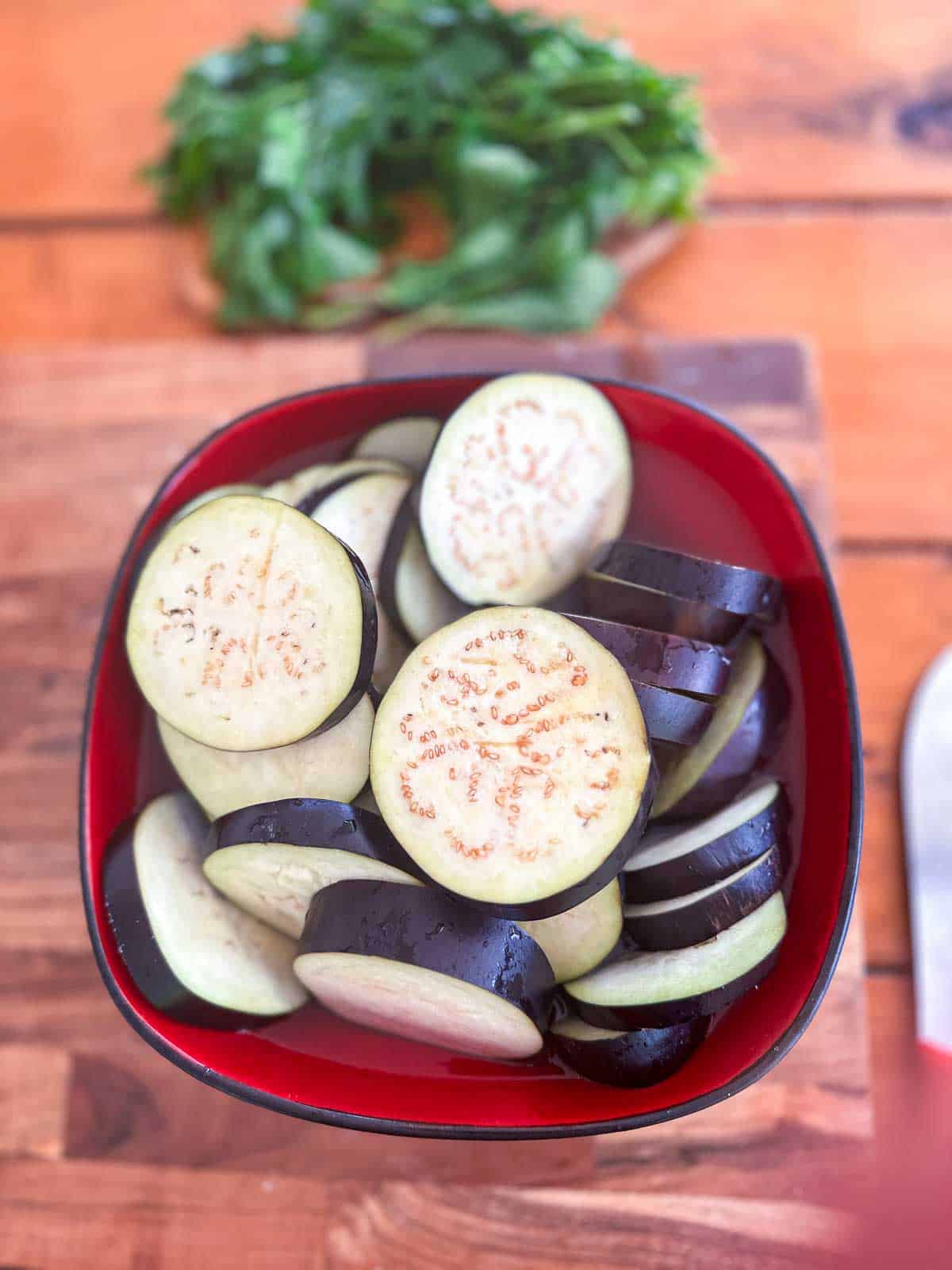Sliced eggplants in a red bowl with water.