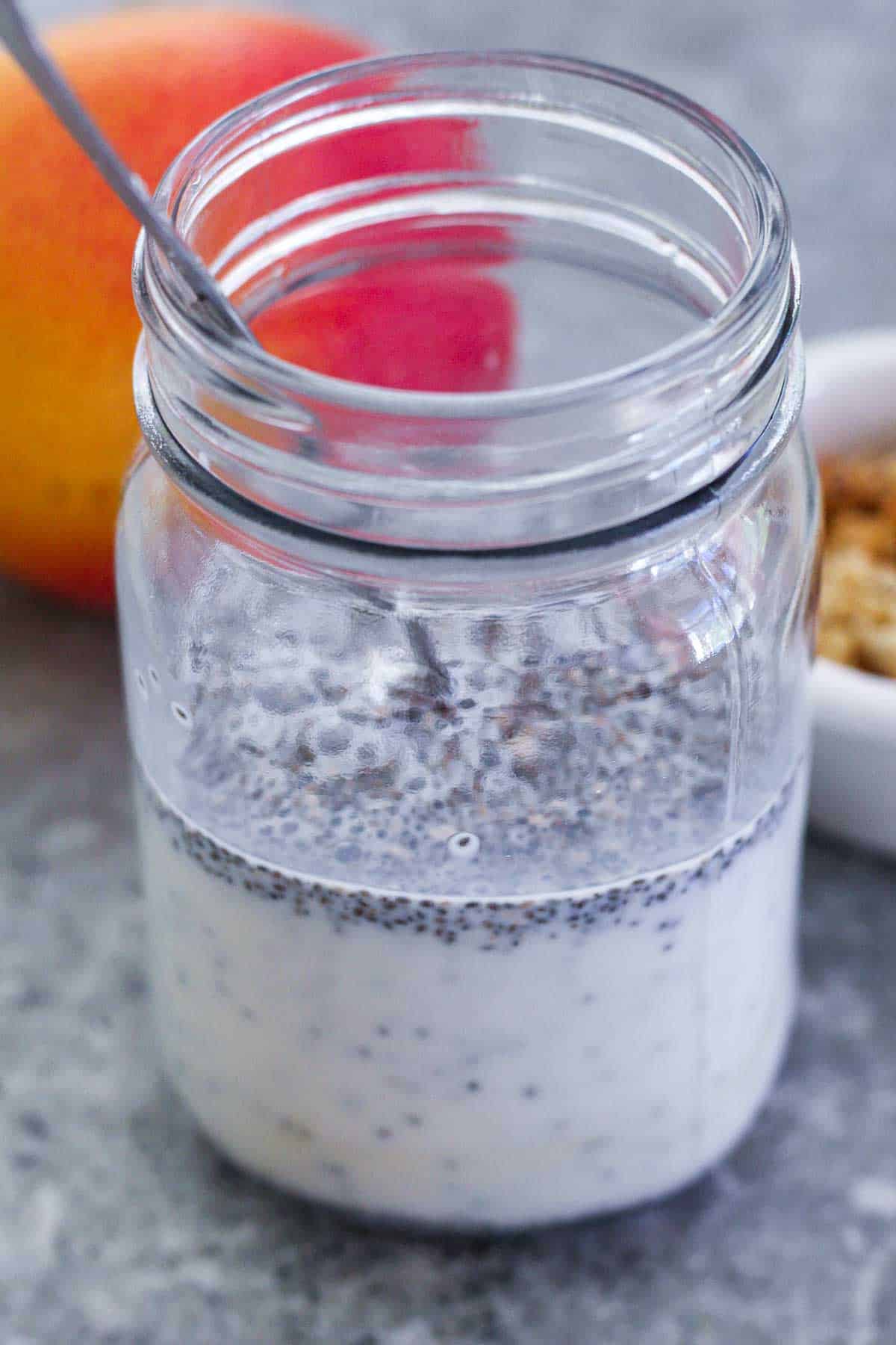 Chia seeds mixed with milk and maple syrup in a mason jar with the spoon still in.

