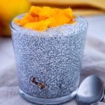 A serving glass with chia seeds pudding over granola, topped with fresh mango.