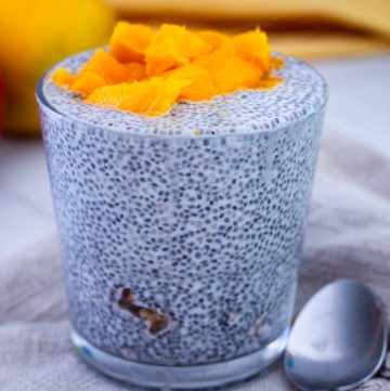 A serving glass with chia seeds pudding over granola, topped with fresh mango.