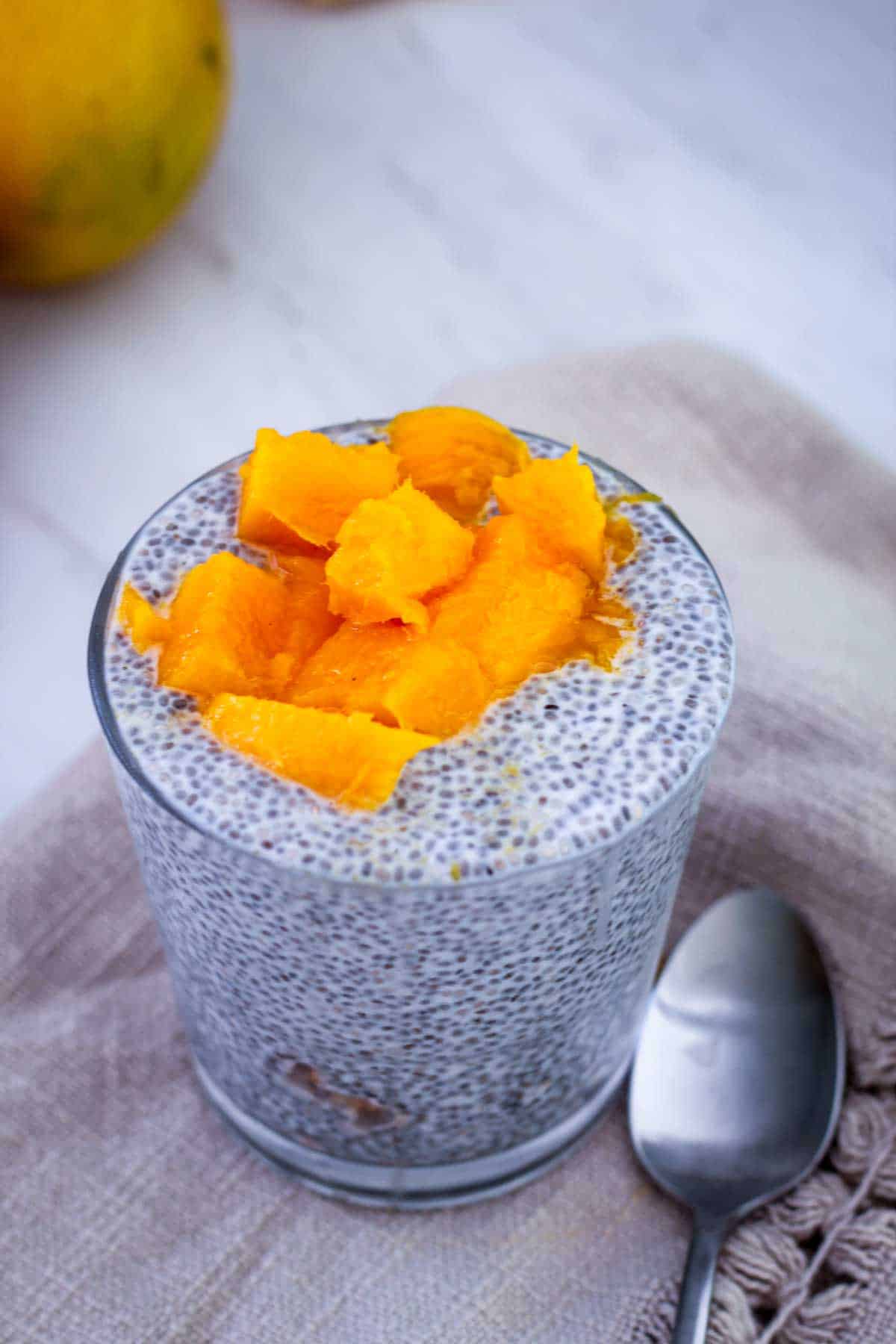 A serving glass with chia pudding and topped off with fresh mango.