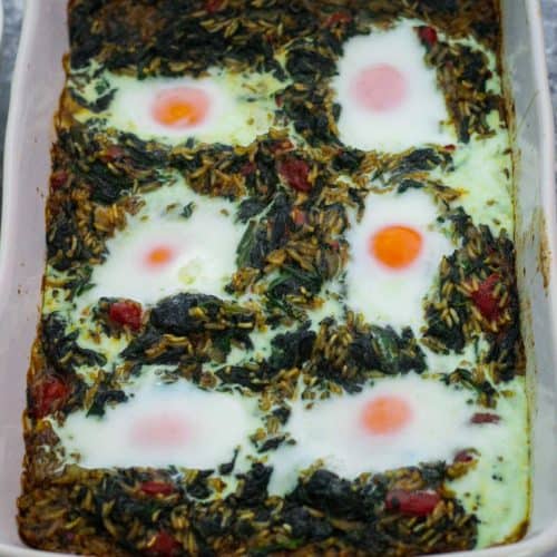 A baking dish showing a baked casserole made with spinach and rice and topped with eggs.
