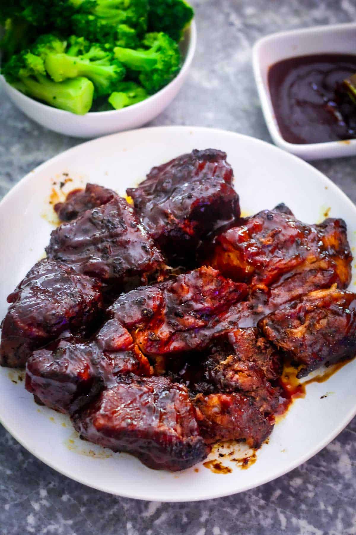 Boneless ribs slathered with bbq sauce are shown on a platter. In the background there are broccoli and more bbq sauce.