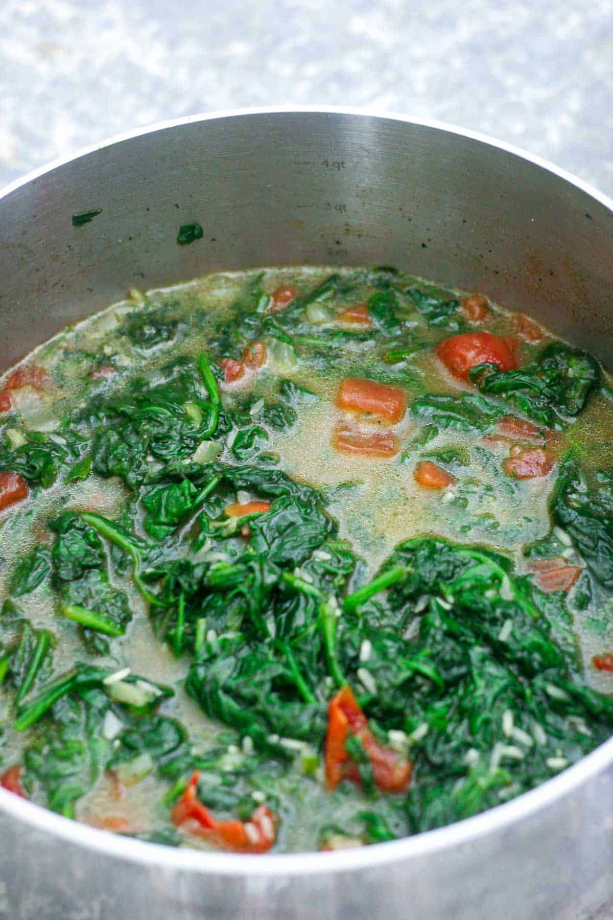 Spinach and rice cooking in the pot, you can see the tomatoes and liquid around the ingredients.