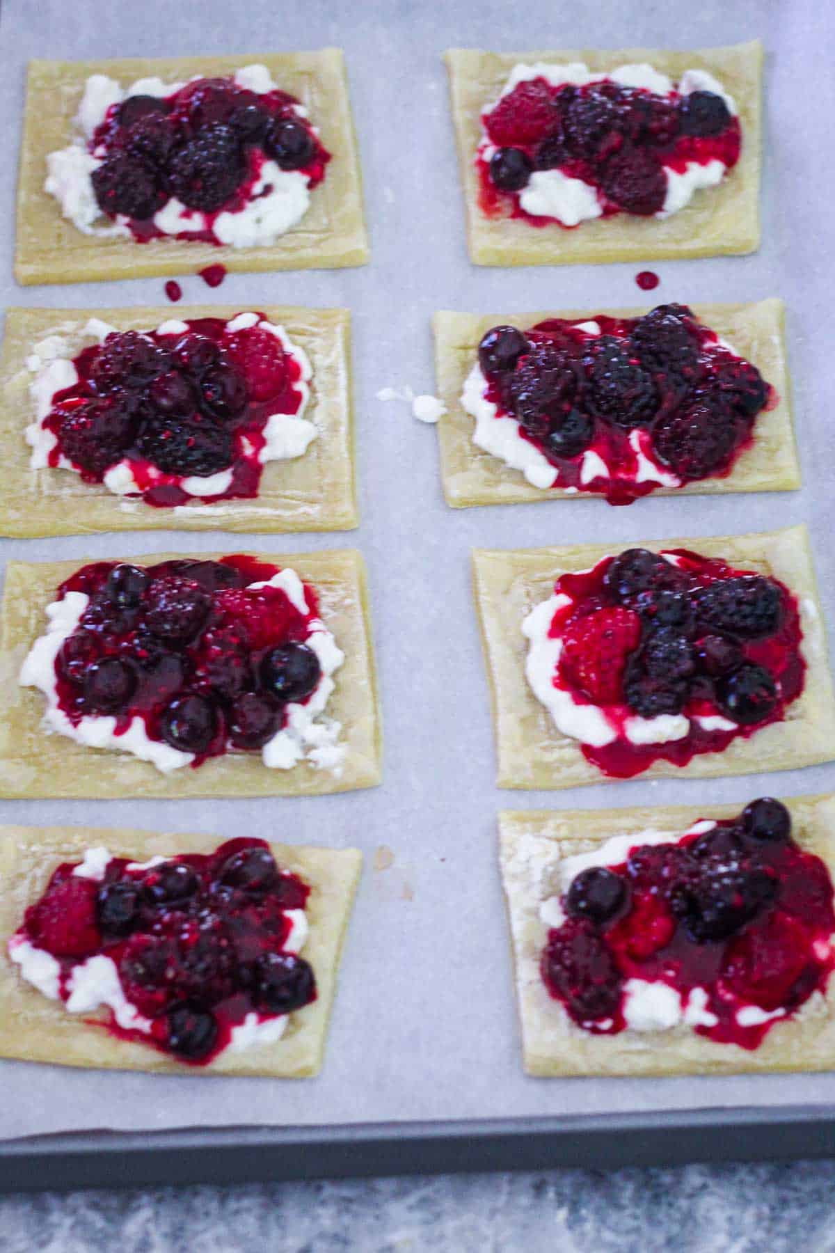 Puff pastry tarts shown with cottage cheese on top and mixed berries filling, before baking. 