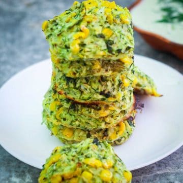 Piled up zucchini and corn fritters on a plate.