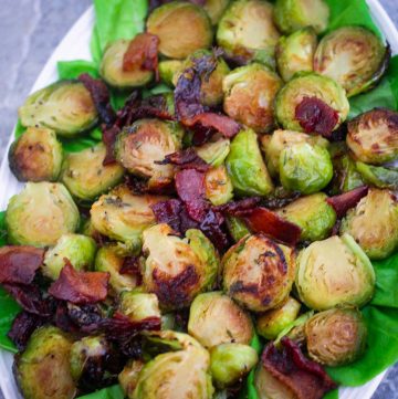 A platter of roasted brussel sprouts with bacon served over leafs of lettuce.