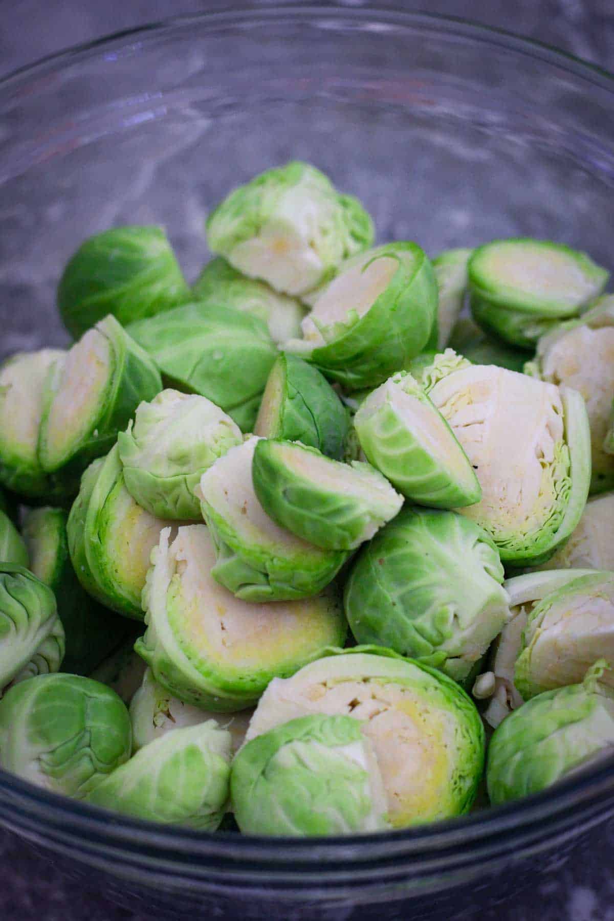 Marinating Brussel sprouts in a mixing bowl with olive oil, maple syrup and seasonings. 