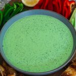 A green deep in a round plate, surrounded by peppers, celery, toasted bread etc.