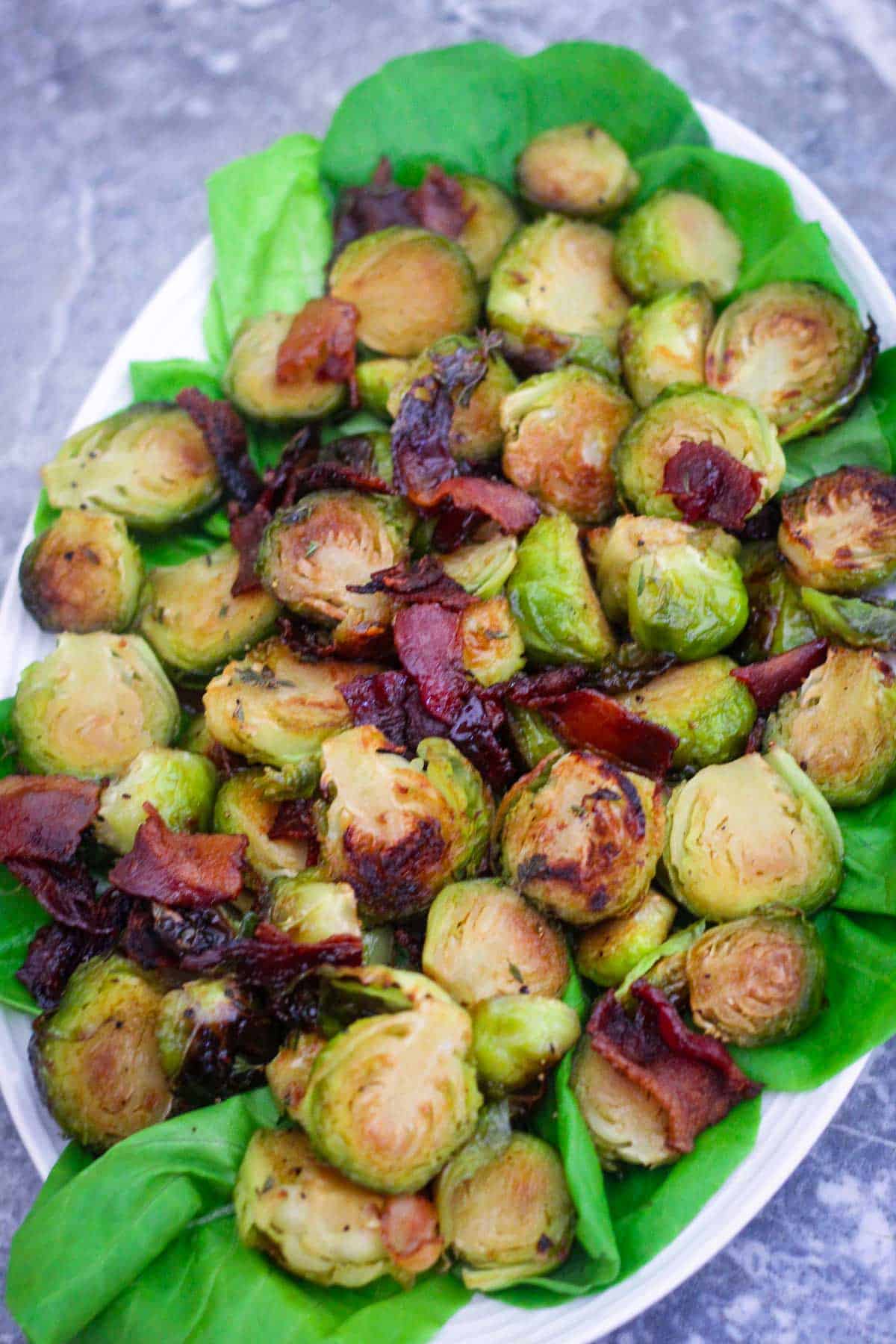 An oval platter shown lined up with lettuce and serving roasted brussel sprouts with bacon. 