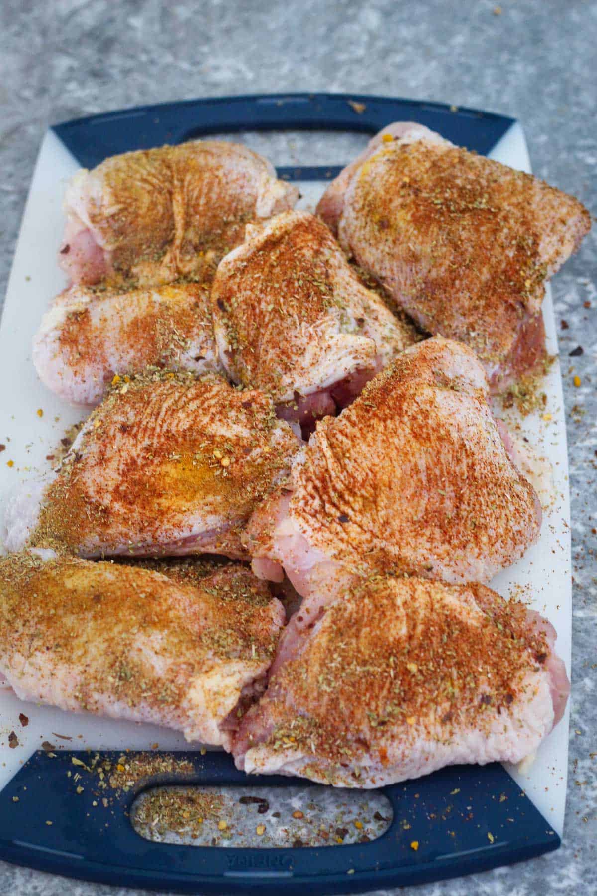 Seasoned chicken with the mix of spices. Chicken thighs are placed over a cutting board.