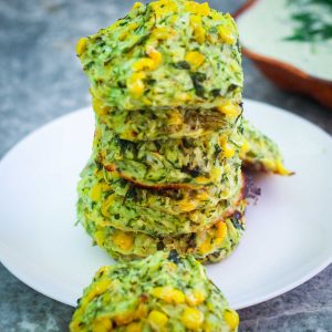 Platter with zucchini and corn fritters with cottage cheese staged in a tower shape over each other.