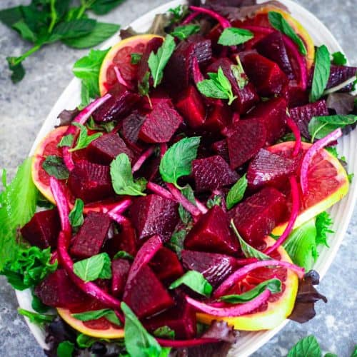 A platter showing a beets and oranges salad over greens. It's a vibrant and beautiful salad.
