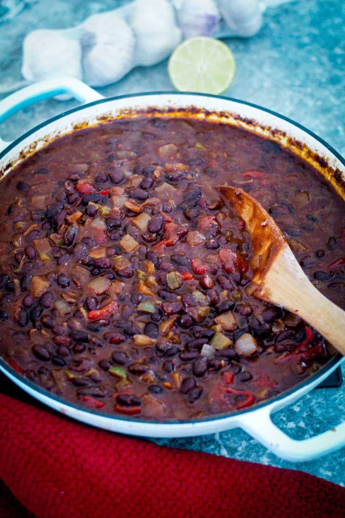A pot with cooked Cuban Black Beans shown with a wooden spoon lifting some up.
