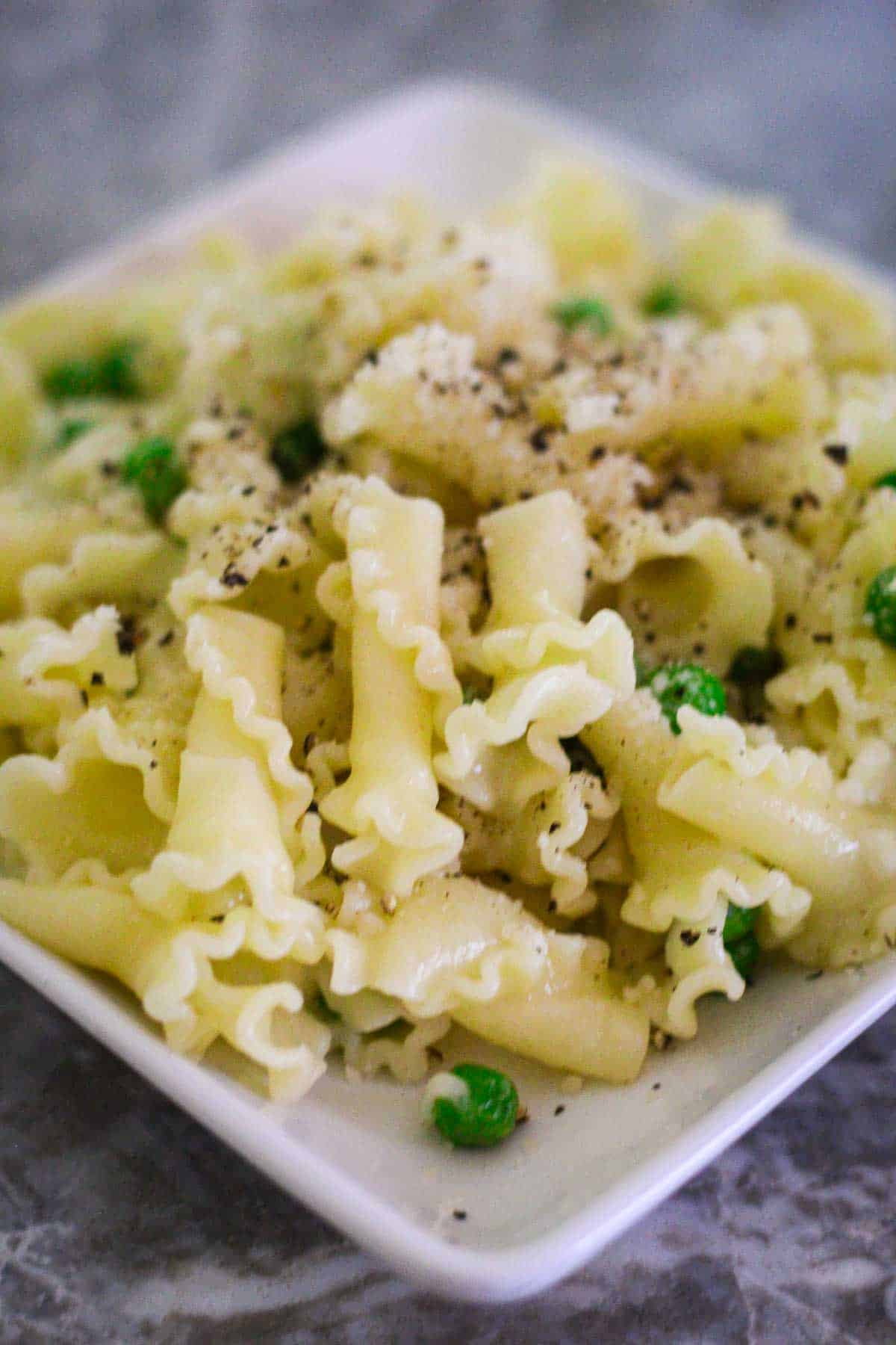 A close up of a pasta dinner plate, showing gigli pasta with peas, topped with freshly grated cheese and black pepper. 
