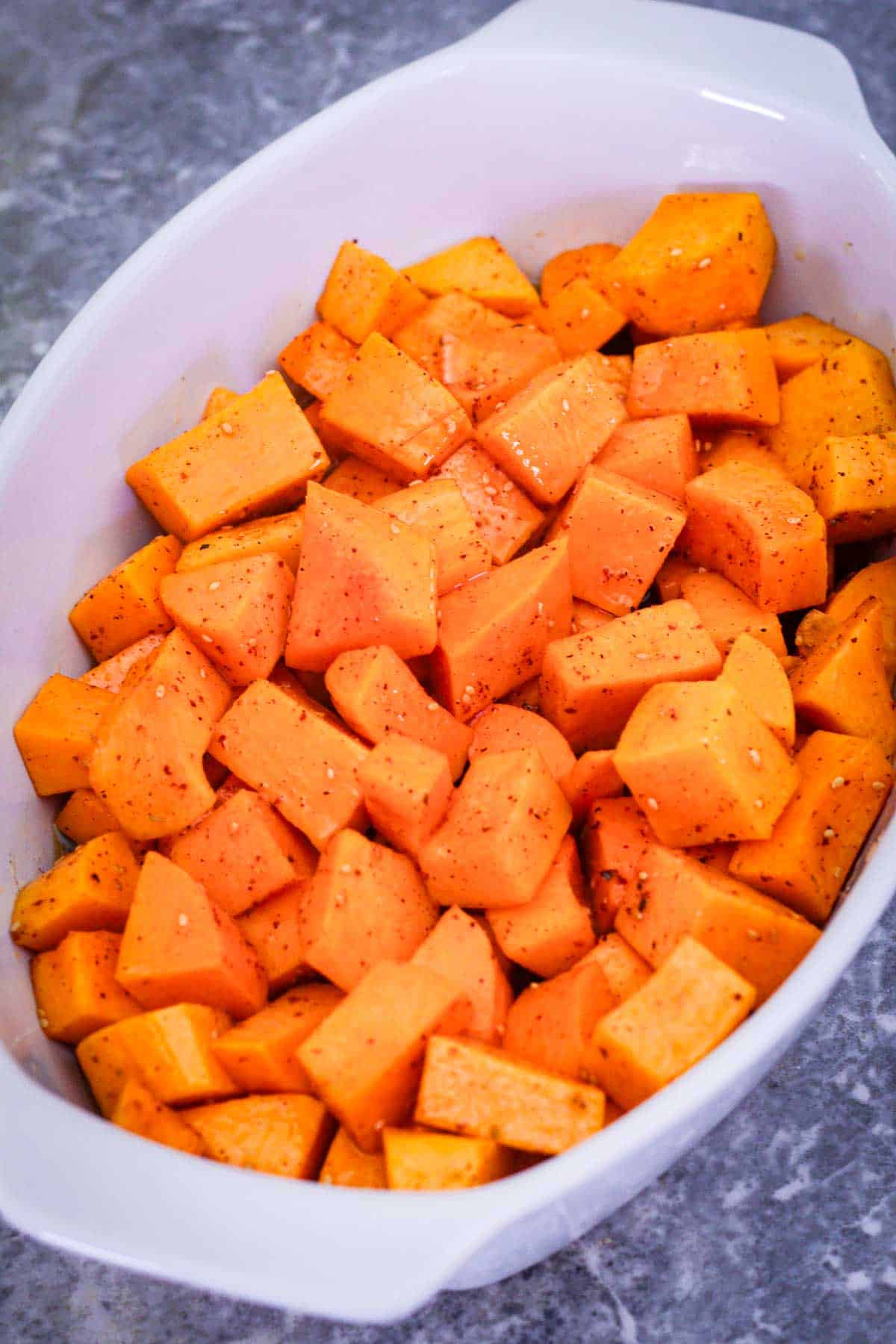 A baking dish showing marinated chunk of butternut squash, right before roasting them.
