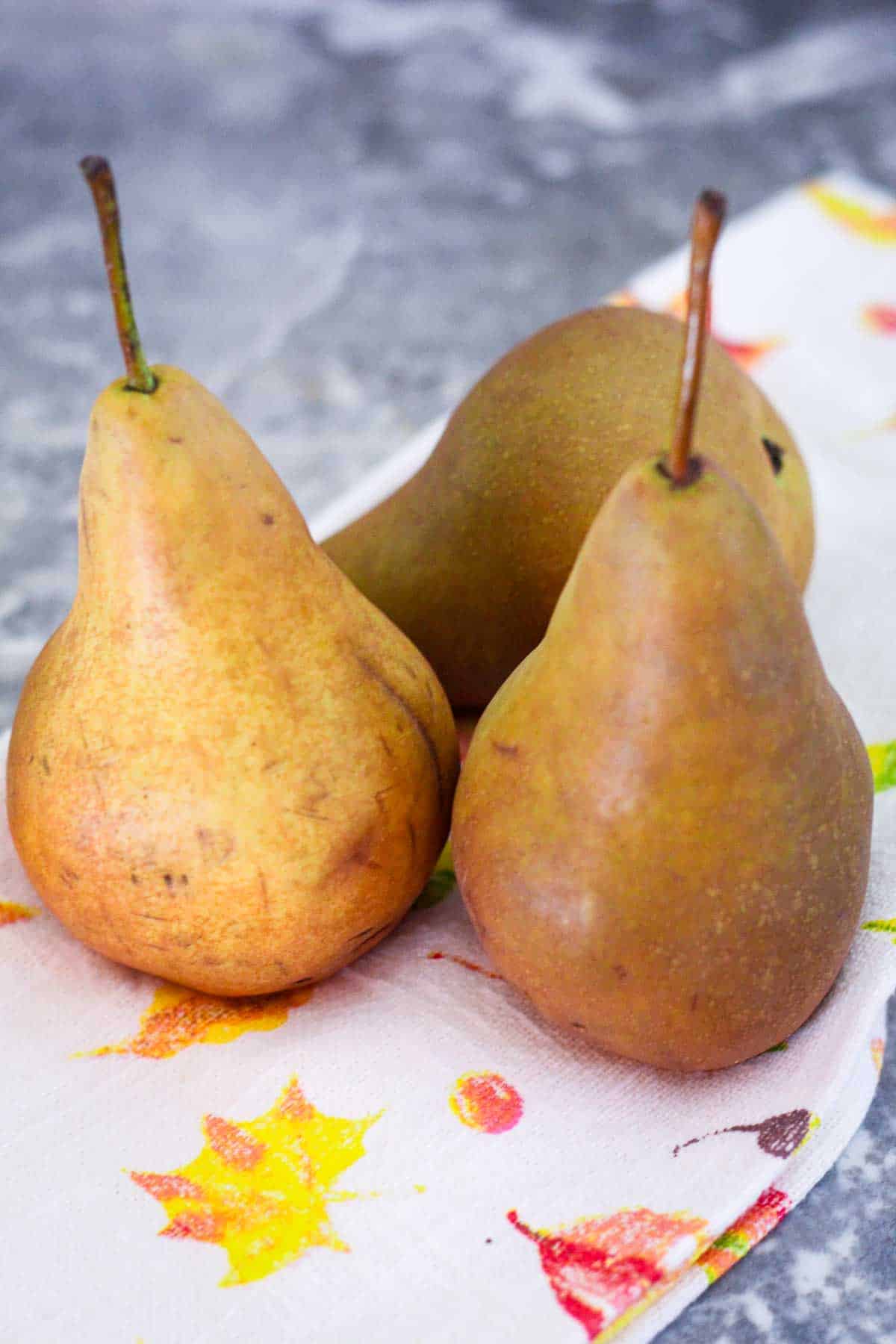 Bosc pears on a counter with a kitchen towel.