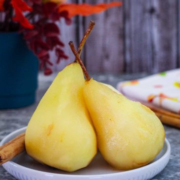 Poached pears shown over a plate with syrup, with a cinammon stick as garnish on the side.