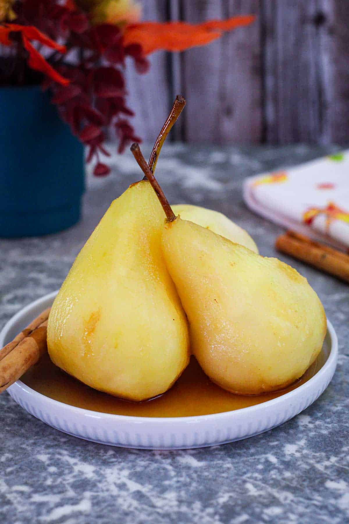 Poached pears in white wine syrup with spices. There's flowers and a kitchen towel in the background.