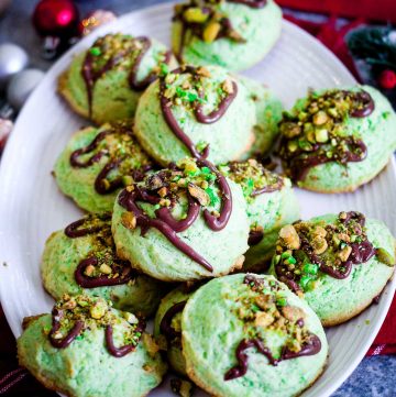 A platter of pistachio cookies covered in melted chocolate and chopped pistachios in a festive setting.