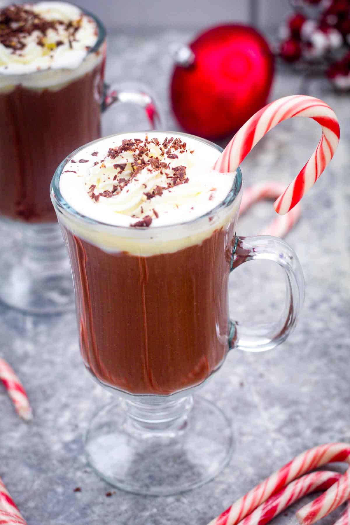 A cup of hot cocoa with whipped cream and toppings served in a festive setting with candy canes.