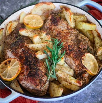 A round baking dish showing baked pork tenderloins, potatoes and lemon and rosemary garnishes.
