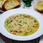 A plate showing star shaped (stelline) soup with veggies and is next to toasted bread and other garnishes.