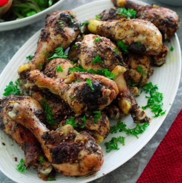 A platter showing baked chicken drumsticks, garnished with parsley.