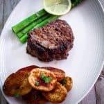 Filet mignon steak, cooked and served on a platter with asparagus, potatoes and garnishes.