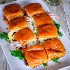 A platter showing 8 buffalo chicken sliders with slaw and other ingredients.