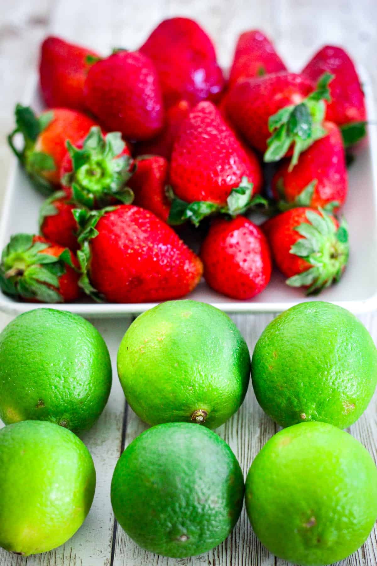 Fresh ripe strawberries and fresh limes lined up on a counter. 