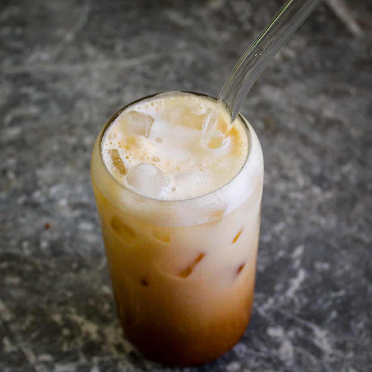 A view from above of a shaken espresso drink over ice with milk and foam. Drink has a glass straw in it.