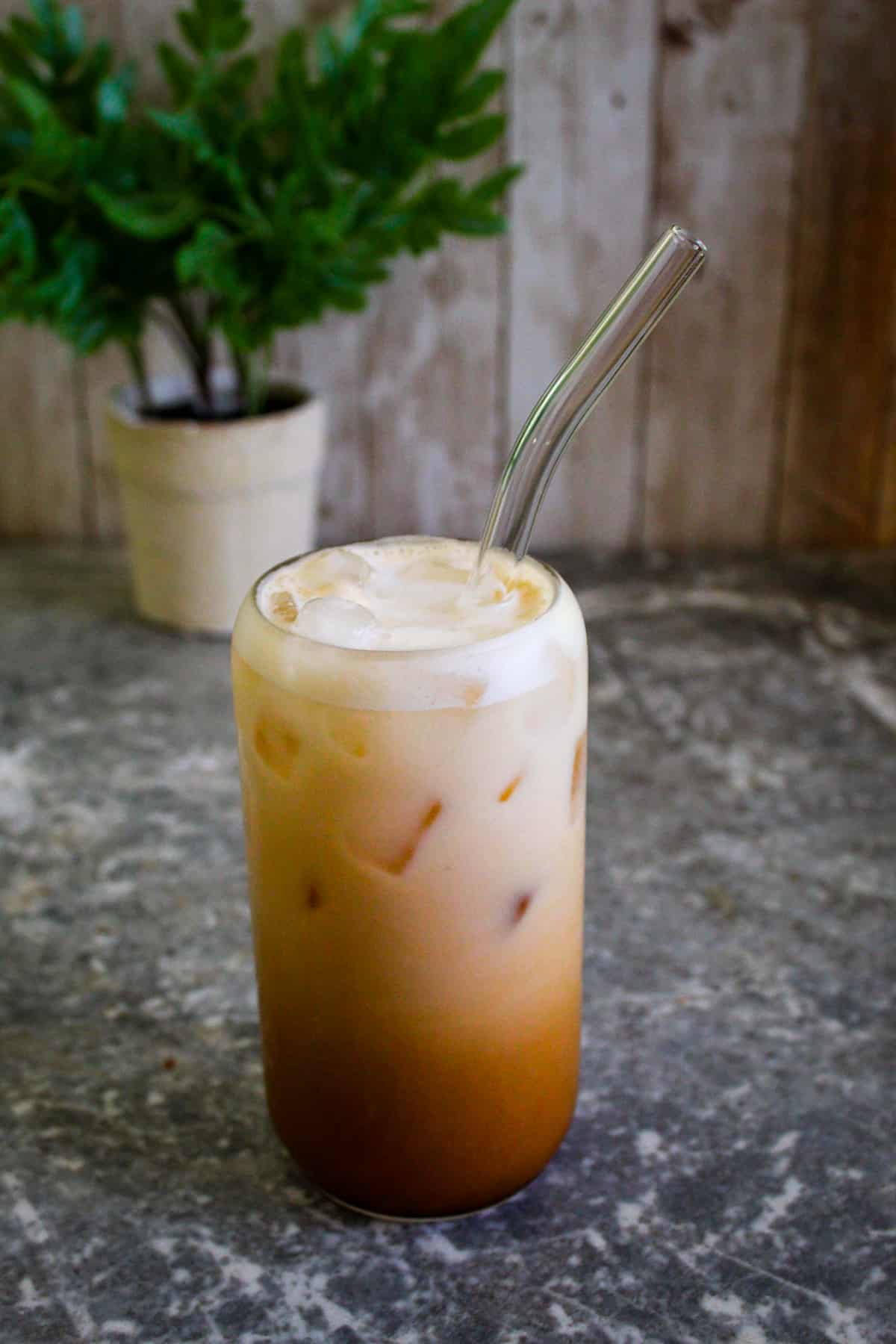 Shaken espresso on a glass cup with ice, milk and a glass straw in it. 