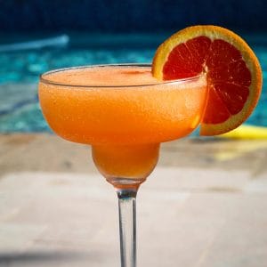 A glass with frozen aperol spritz in front of the pool