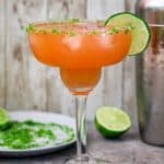 A margarita glass with guava margarita, garnished with lime slice.