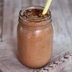 A jar with a blended smoothie shown on a countertop, with a yellow straw in it.