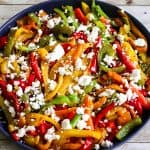 A platter with stir fried bell peppers of different colors, cut in strips. Peppers are then topped with crumbles of feta cheese.