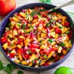 A blue bowl with peach salsa and fresh peaches, cilantro and lime around the bowl.