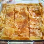 A glass baking dish showing a phyllo pie, just baked, cut in squares.