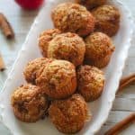 A plate with apple muffins garnished with cinnamon sticks & apples.
