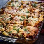 Baked ziti casserole cut in squares, garnished with parsley and shown on a glass rectangular dish.