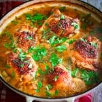Chicken thighs cooked in a Dutch oven with veggies, broth and garnished with greens.