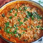 A pot of cooked orzo with tomatoes, parmesan and spinach. Dish is garnished with fresh parsley.